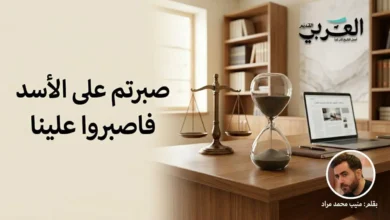 صورة تعبيرية لمكتب صحفي يضم ساعة رملية وميزان عدالة، مع صورة الكاتب منيب محمد مراد وشعار الموقع، ومكتوب عليها عبارة "صبرتم على الأسد فاصبروا علينا". تعبر عن مقالة سياسية حول المرحلة الانتقالية في سوريا.